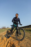 Fototapeta  - Cyclist in shorts and jersey on a modern carbon hardtail bike with an air suspension fork standing on a cliff against the background of fresh green spring forest