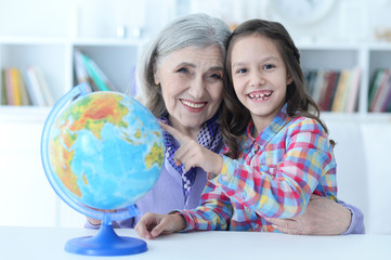 Poster - Smiling grandmother and granddaughter sitting at table with globe