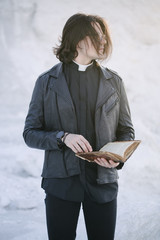 Wall Mural - Young priest portrait outside at sunset. He is wearig eye glasses and roman collar shirt and a leather jacket.