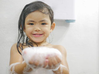 Little baby girl, 3 years old, feels proud of making a lot of soap foam / bubbles in a bathroom at home - children and a bubble bath