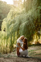 Beautiful girl 7 years old with long blonde hair with a blonde mom walk and cuddle at sunset in the summer park