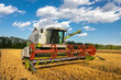 © dechevm - modern combine (harvester)  harvesting on wheat field, cloudy sky