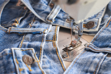 Wall Mural - Needle presser foot with thread of white industrial sewing machine with blue jeans close-up.