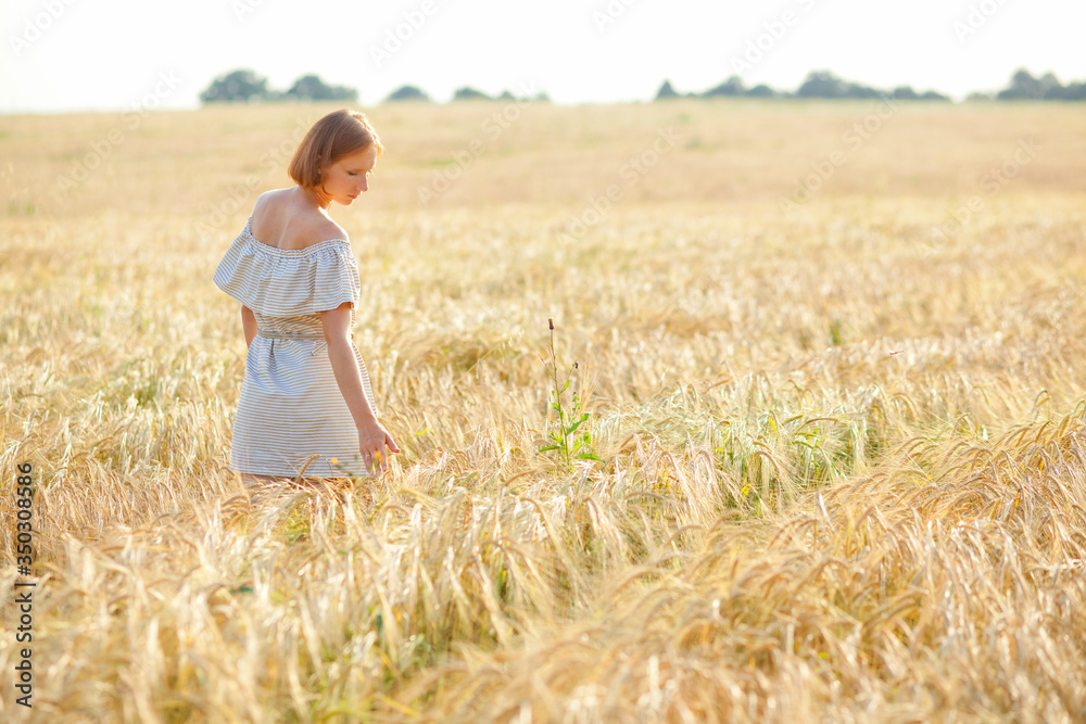 A young girl with a straw hat on her head is dancing in a wheat field ...