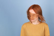 Young girl in yellow t hsirt shaking her red hair. Frontal up body view on blue background