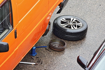 Wall Mural - Removed wheel and brake drum are lying on the road next to the orange minibus on a hydraulic Jack, overheating the jammed car brakes on the way