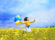 Jumping teenager girl in a field with airy blue and yellow balloons. A blue sky and a yellow field with blooming rapeseed.The concept of freedom and celebration. Girl's birthday