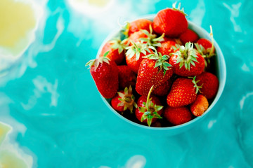 red juicy ripe strawberries in a blue vase on a light background on a blue stand made of epoxy resin. Healthy spring breakfast, fruit plate.