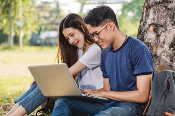 Wall Mural - Young man and girls friend classmates sitting at park under tree