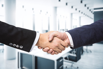 Handshake of two businessmen on the background of modern furnished office, partnership concept, close up