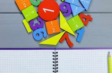 Colorful math fractions, numbers on open notebook and pencils on gray wooden background. Interesting, fun mathematics for kids. Education, back to school concept	