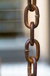 Links of old rusty metal chain, which hanging in the air, close-up on a blurry background. Pattern of an iron weathered chain rusted through with a textured surface and yellow orange streaks of rust