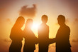 © NAKHARIN - Silhouette of business teamwork and happy of success in sunset evening sky background.