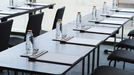 plastic water bottles, drinking glasses with pencil and white papers setup on the table prepared for