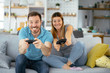 © JustLife - Husband and wife playing video game with joysticks in living room. Loving couple are playing video games at home.