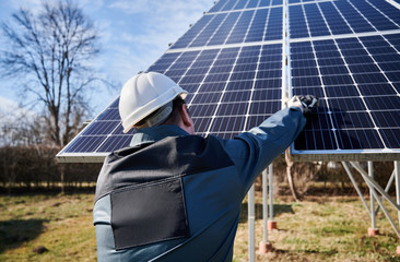 Wall Mural - Rear view of a worker in coverall, white helmet and working gloves, standing with his back to camera, fastening solar modules together. Concept of alternative energy and power sustainable resources.