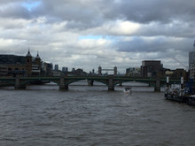 Bridges Over Thames River Amidst Buildings Against Cloudy Sky