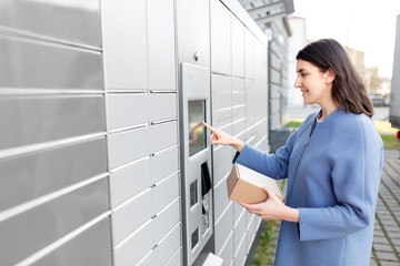 mail delivery and post service concept - happy smiling woman with box at outdoor automated parcel machine choosing operation on touch screen