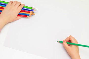 Sticker - Top view of girl's hand drawing by green pencil on white sheet of paper holding bunch of colored pencils in her hand. Selective focus.