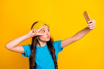 Sticker - Photo of funny little lady hold telephone quarantine time stay home talk skype classmates show v-sign near eye send kisses wear casual blue t-shirt headband isolated yellow color background