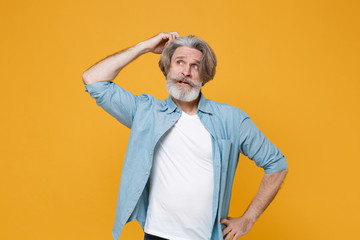 Preoccupied elderly gray-haired mustache bearded man in casual blue shirt posing isolated on yellow background studio portrait. People emotions lifestyle concept. Mock up copy space. Put hand on head.