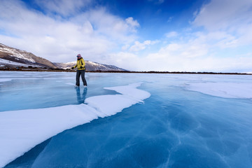 A girl in a yellow jacket and ice skates stands on the blue lake of lake Baikal