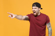 © ViDi Studio - Irritated angry young bearded tattooed man guy in casual t-shirt black cap isolated on yellow background. People lifestyle concept. Mock up copy space. Pointing index finger aside, screaming swearing.
