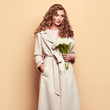 © Oleg Gekman - Young elegant woman in trendy white coat. Blonde hair, coral dress, isolated on beige background, studio shot. Fashion spring lookbook. Model woman with white tulips