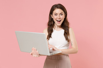 Excited young brunette woman girl in light casual clothes posing isolated on pastel pink wall background studio portrait. People lifestyle concept. Mock up copy space. Working on laptop pc computer.
