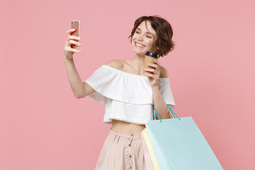 Smiling young woman girl in summer clothes isolated on pink background studio. Shopping discount sale concept. Hold package bag with purchases, cup of coffee or tea, doing selfie shot on mobile phone.