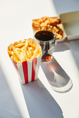 Wall Mural - selective focus of tasty deep fried chicken, french fries and soda in glass on white table in sunlight