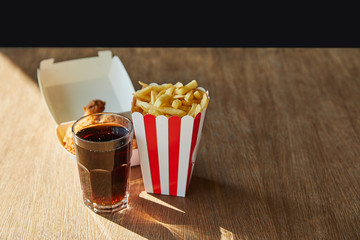 Wall Mural - deep fried chicken, french fries and soda in glass on wooden table in sunlight isolated on black
