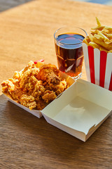 Wall Mural - deep fried chicken, french fries and soda in glass on wooden table in sunlight