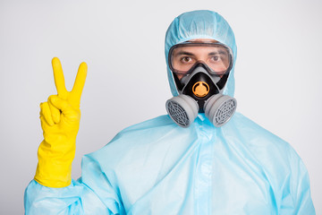 Wall Mural - Portrait of medical worker man in white hazmat uniform breathing mask make v-sign isolated over gray color background