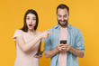 © ViDi Studio - Shocked funny young couple friends guy girl in casual clothes isolated on yellow background. People lifestyle concept. Mock up copy space. Pointing index finger on mobile phone, typing sms message.