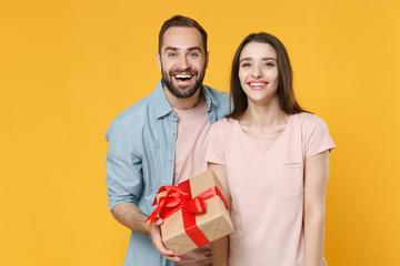 Sticker - Excited young couple two friends guy girl in casual clothes isolated on yellow background. Valentine's Day, International Women's Day, birthday, holiday concept. Hold present box with gift ribbon bow.