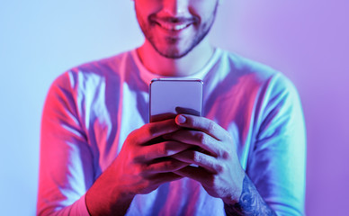 Wall Mural - Millennial man is online. Smiling guy is typing in smartphone