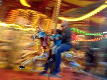 Father And Son Sitting On Horse In Carousel Ride