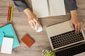 Top view of business table with hands typing on laptop keyboard with color pens, notebooks, business card bag and mouse, on a wooden table to connect with others in the digital technology world.