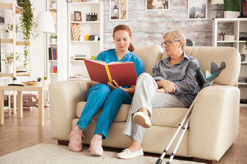 Caucasian female doctor reading a book for old woman in nursing home.