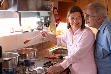 Coppia di anziani felici cucina il pranzo in casa e scherza allegramente con grande feeling