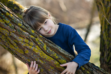 Wall Mural - Portrait of a pretty child girl leaning to a tree trunk in autumn outdoors.