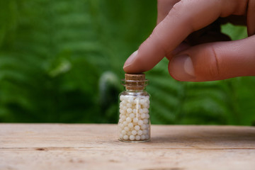 Man holding Bottles of homeopathic globules on green fern background. Homeopathy medicine.