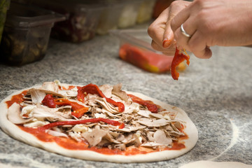 the pizza maker prepares a pizza with porchetta and red peppers