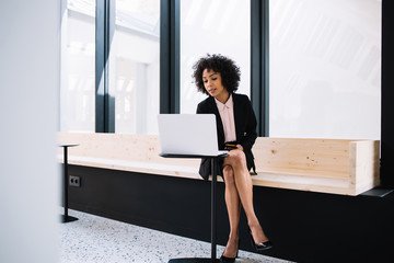 Beautiful dark skinned businesswoman in formal wear reading mail on laptop computer working in modern designed office, confident african american female executive manager using technology for job