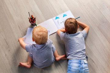 Two little boys drawing on the floor in his room