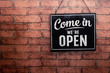© Maderla - Come in we're open, vintage black retro sign in red brick wall.