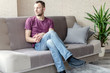 © Sergey - young calm man sits on a sofa in a bright room and looks out the window