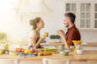 © deniskomarov - Happy loving couple chatting during coffee break standing at home kitchen. Handsome husband and beautiful wife together. Woman in apron cook fresh vegetable salad. Man entertain beloved soulmate