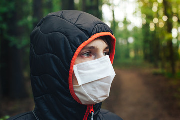 Portrait of a young woman in a medical mask on her face in the forest. The adult female covered her face with a mask to protect herself from diseases.